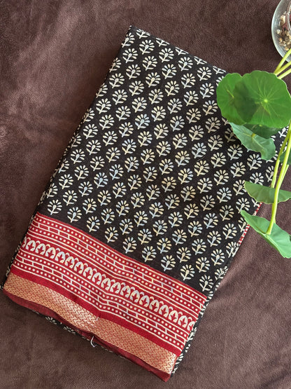 Kunkuma_Ajrakh Print Saree from saree from thambai .Black fabric with white floral pattern on a brown surface