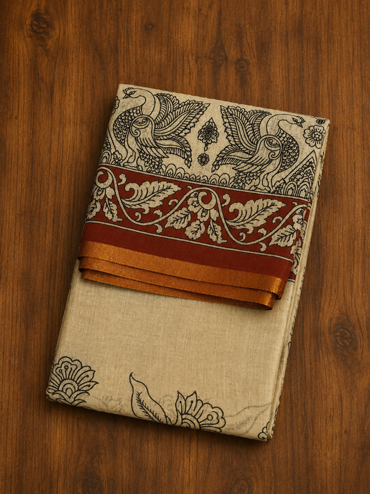 A neatly folded off-white linen silk saree from Saree from  Thambai online store, displayed on a wooden surface. The body of the saree has a slubbed textured finish with black floral line art at the bottom. The pallu showcases traditional kalamkari-style peacock and floral prints, bordered by a rich maroon band and a subtle copper gold zari trim.