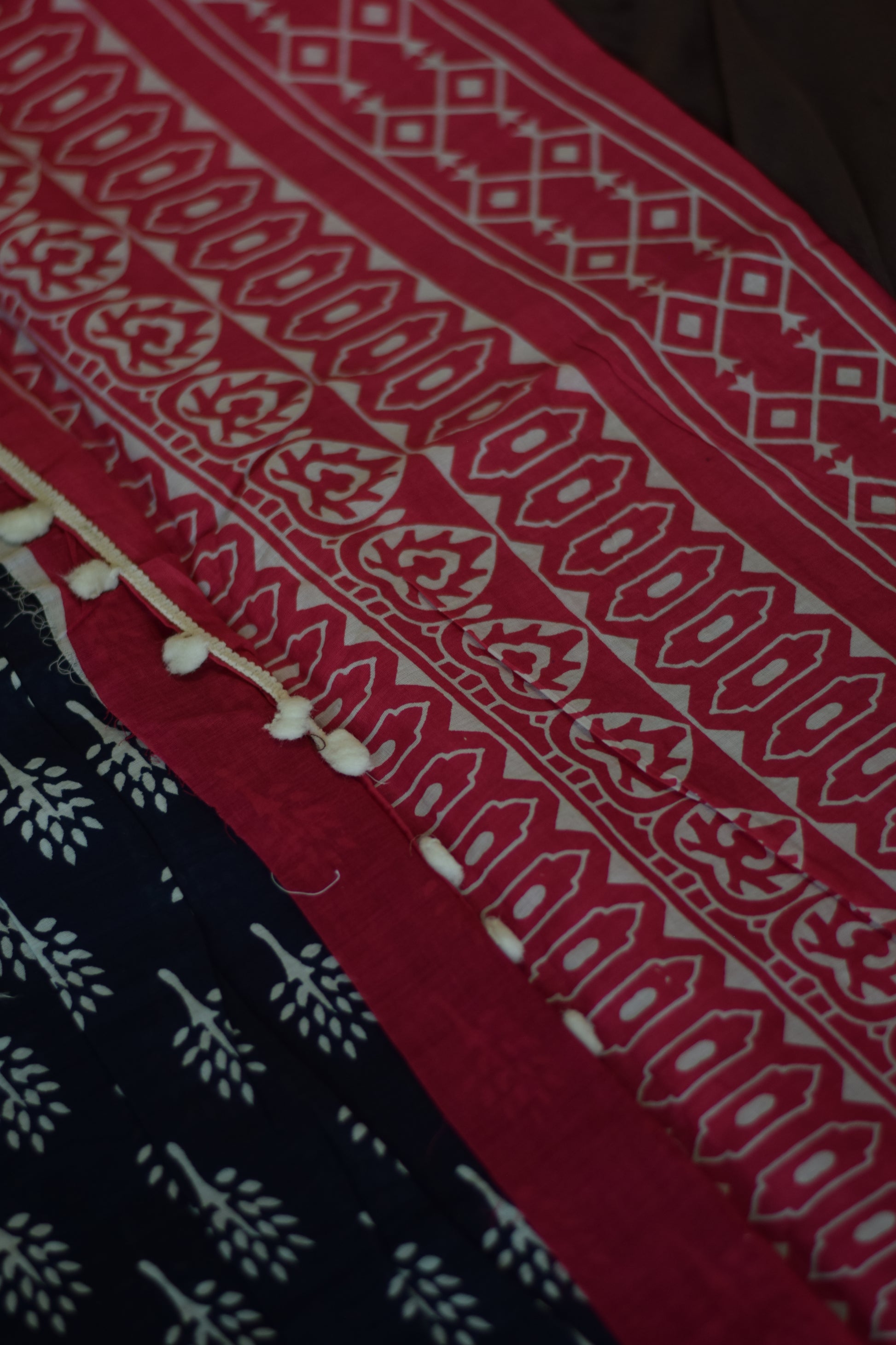 Close-up of Mandhara_Bagru print mul mul cotton saree from saree from thambai.pink and navy patterned fabric on a brown surface 