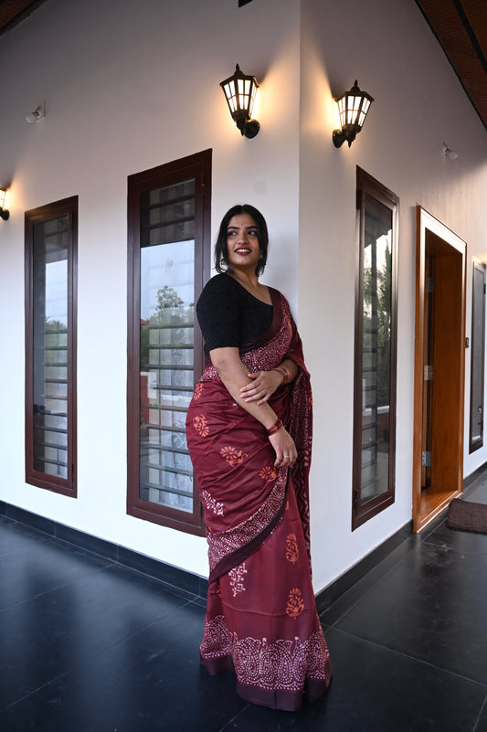 Woman in a Sindoora_Chungudi Saree from saree from thambai standing in a modern interior setting with large windows.