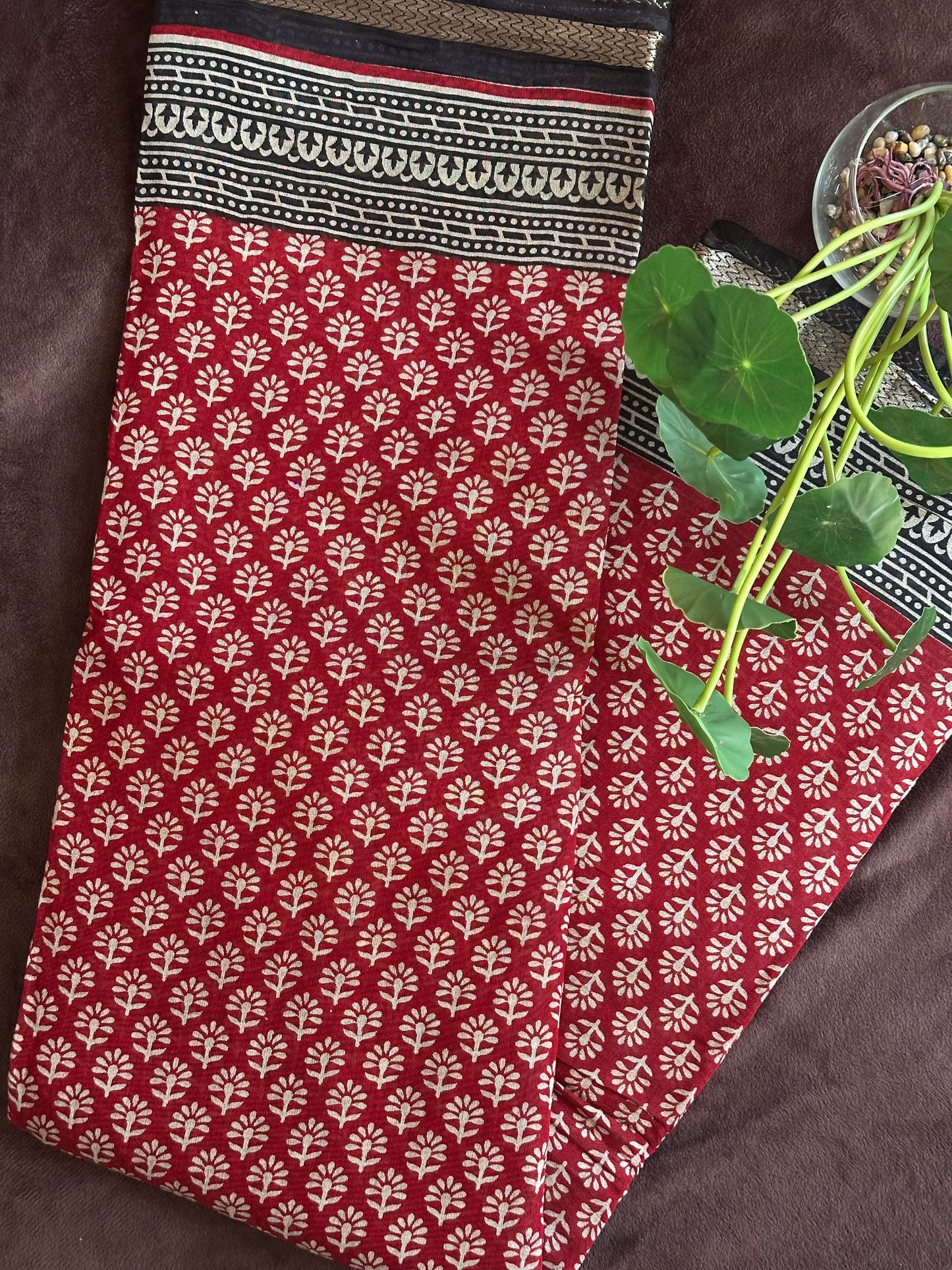 Kunkuma_Ajrakh Print Saree from saree from thambai .Red fabric with white floral pattern on a brown surface
