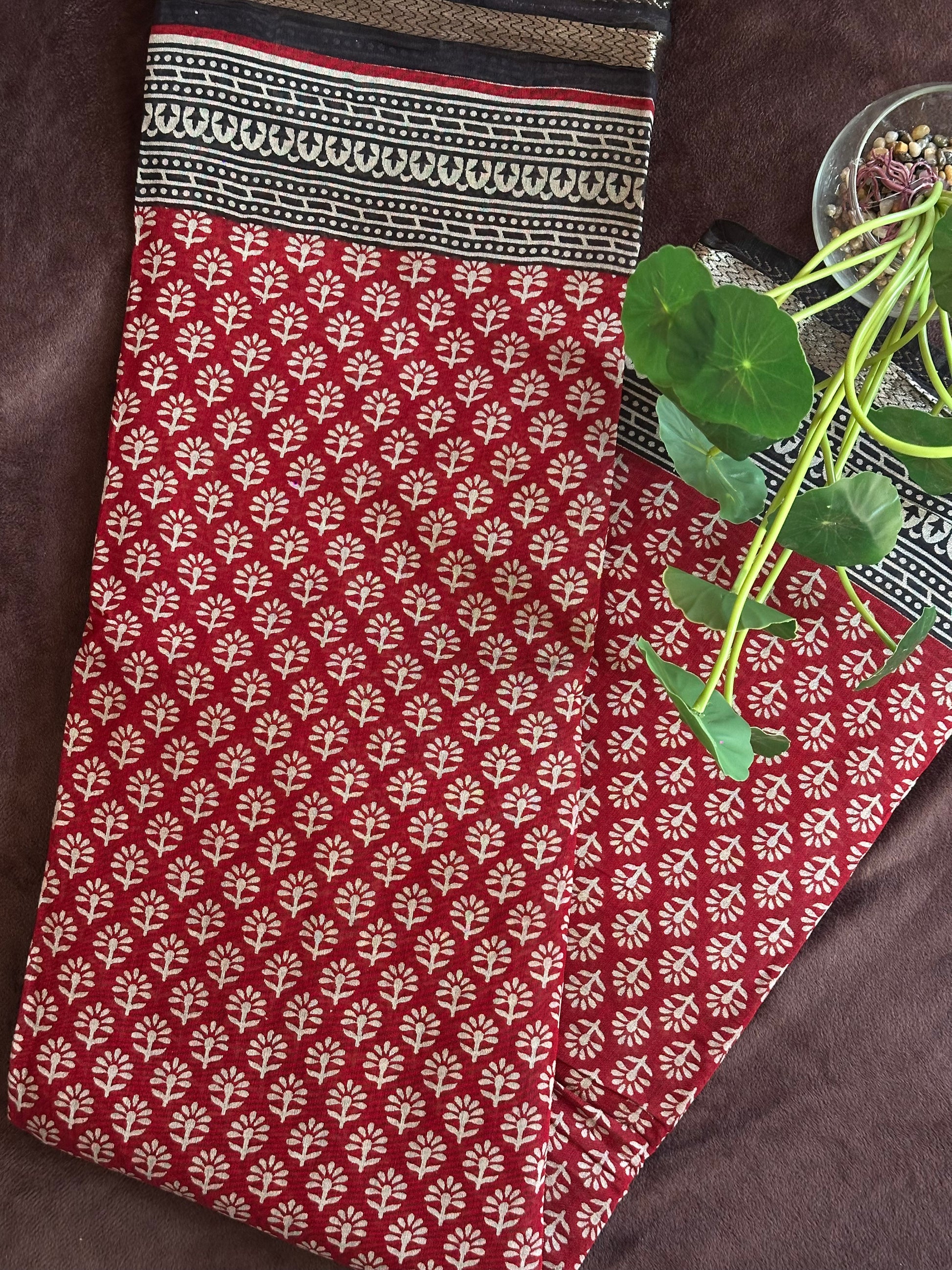 Kunkuma_Ajrakh Print Saree from saree from thambai .Red fabric with white floral pattern on a brown surface