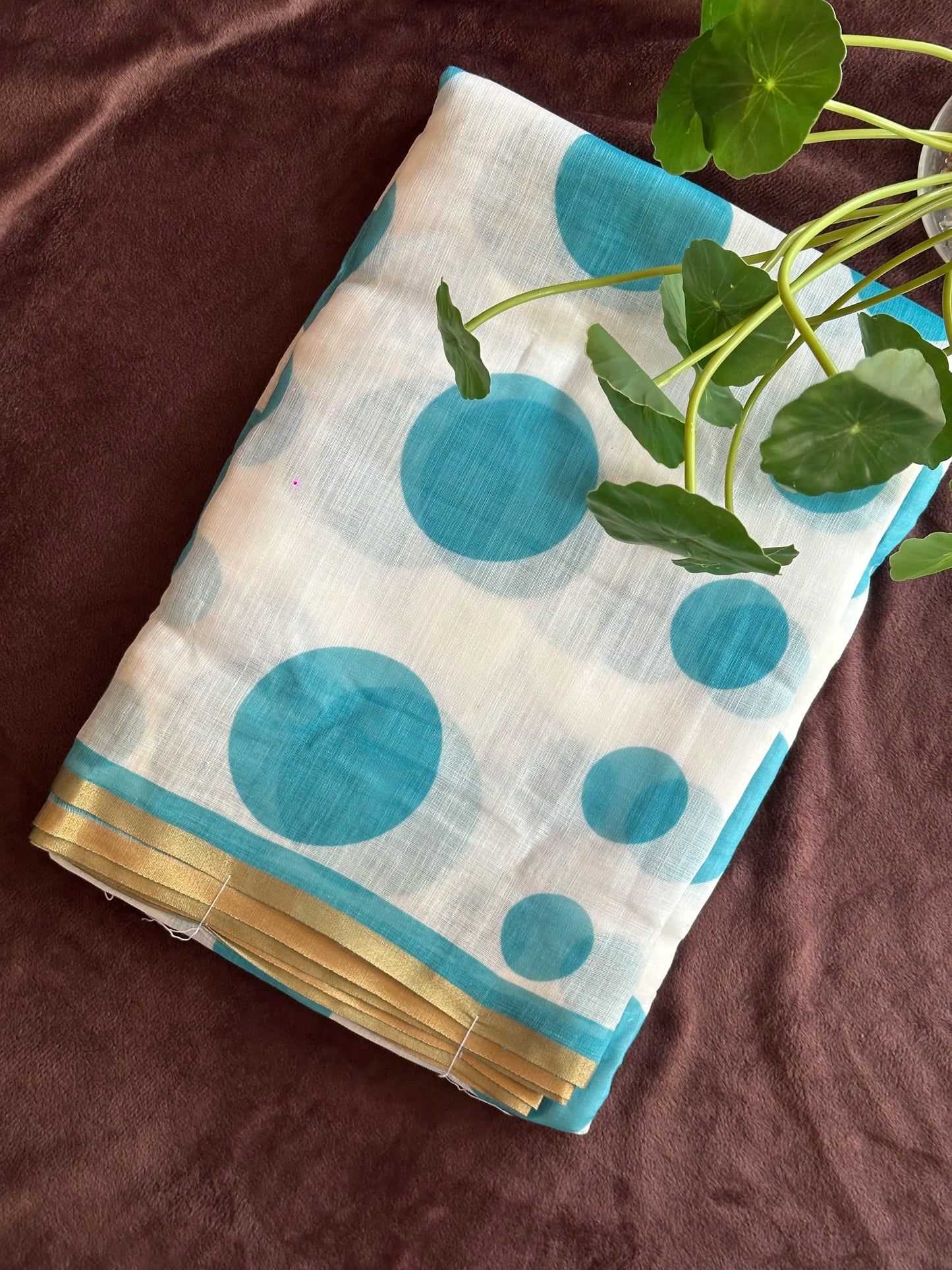 Ambili_Polka dot print semi-linen cotton saree in blue polka dots and gold border on a brown surface