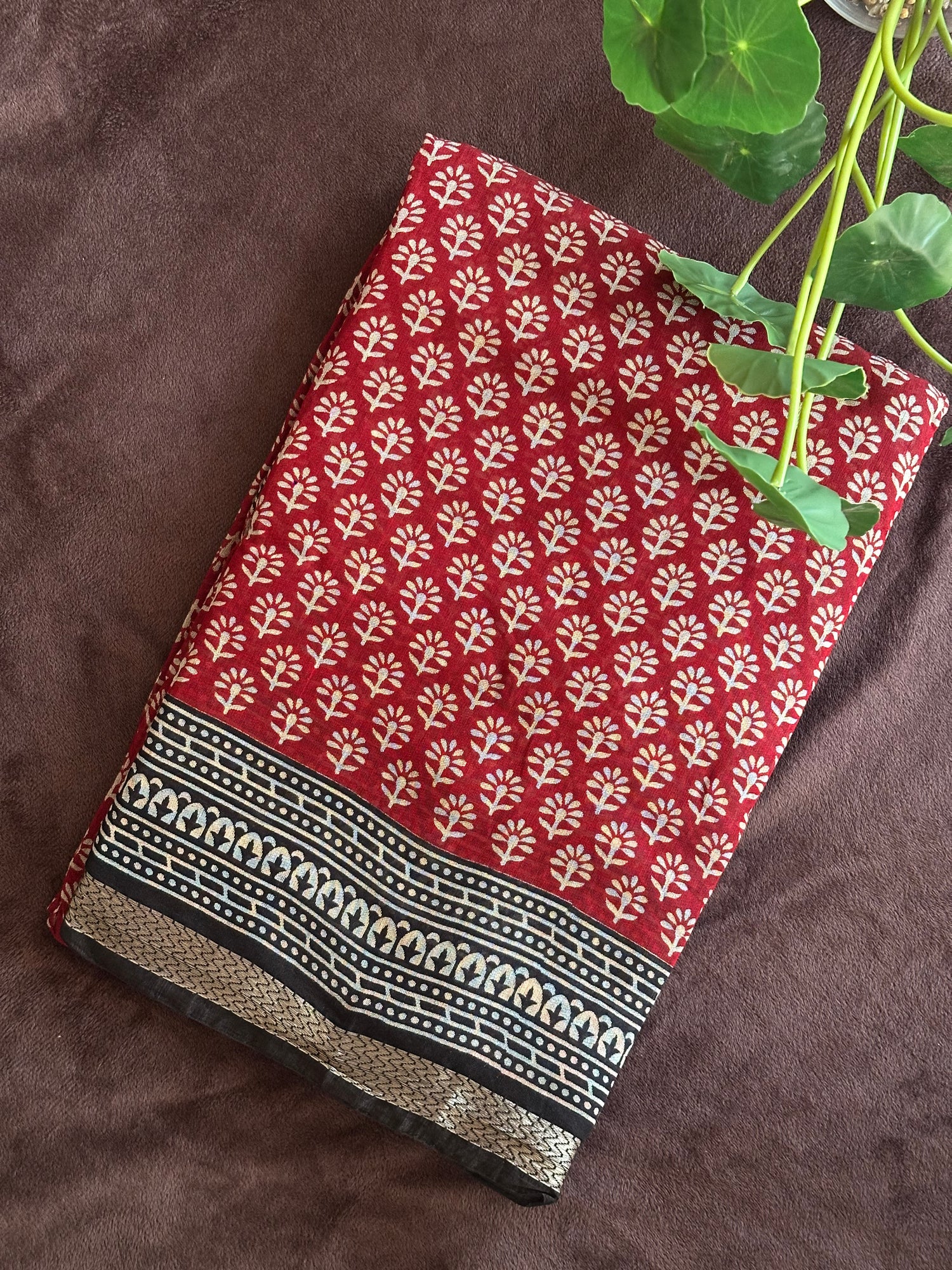 Kunkuma_Ajrakh Print Saree from saree from thambai .Red fabric with white floral pattern on a brown surface