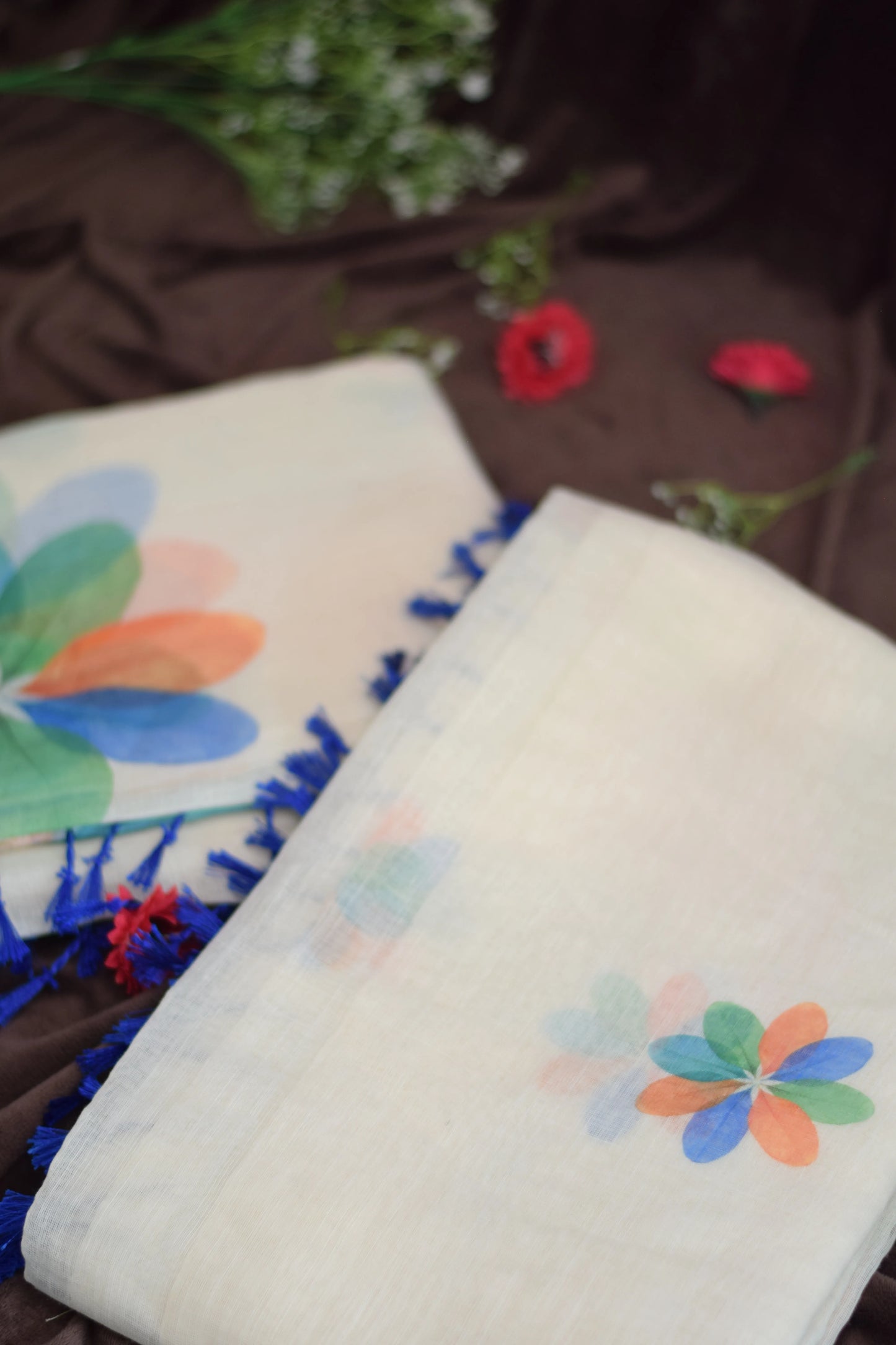 Thennal_Ice cream saree -Abstract Overlapping Petals_saree from thambai.Two scarves with colorful floral patterns and blue tassels on a brown fabric background.
