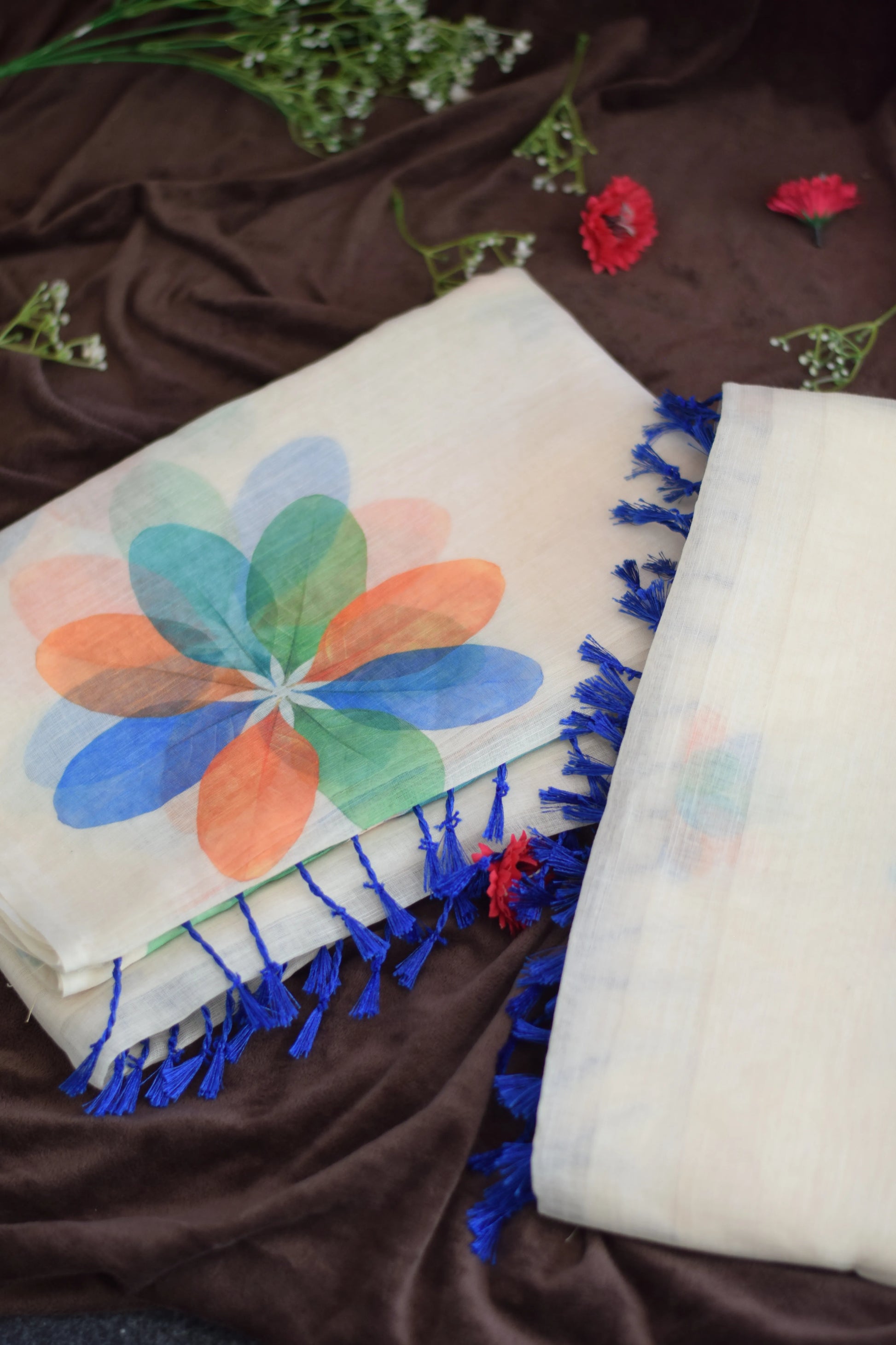 Thennal_Ice cream saree -Abstract Overlapping Petals_.Two scarves with colorful floral patterns and blue tassels on a brown fabric background.