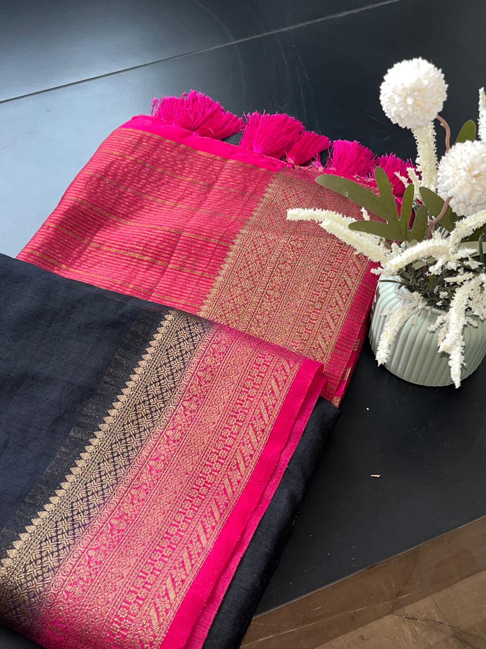 Varmukil Jute Linen Cotton saree with pink and black combo on a dark surface with white flowers.